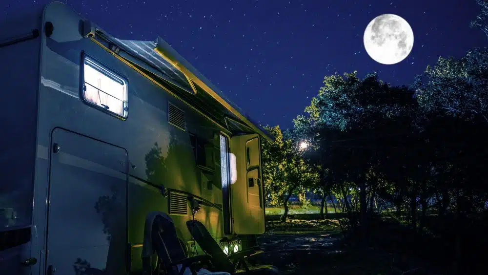 Parked RV with chairs outside under a full moon.