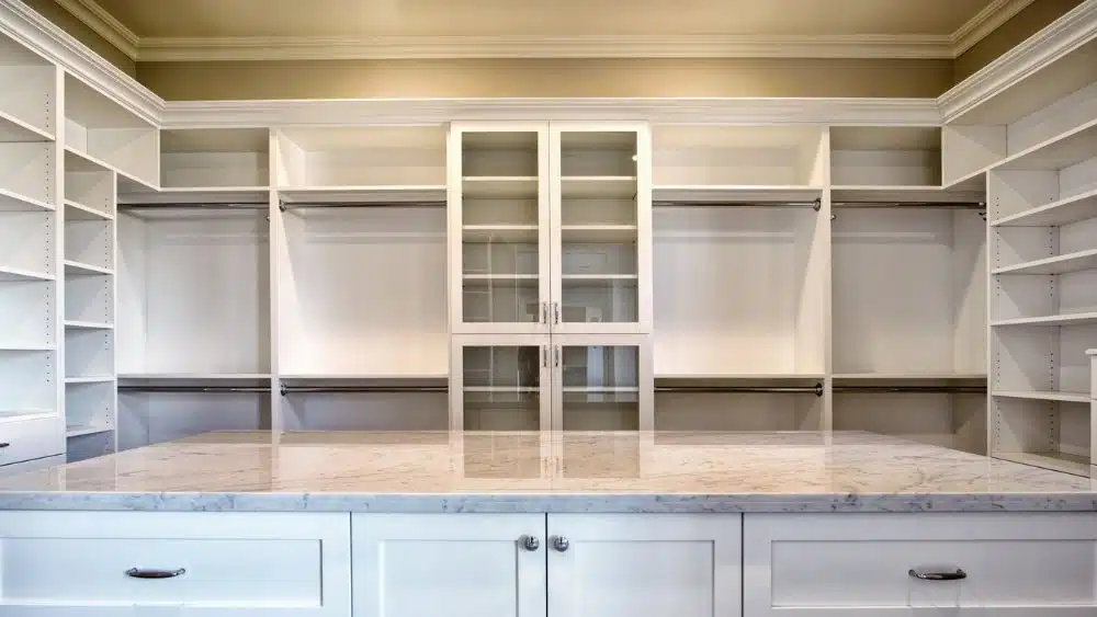Huge walk-in closet with hanging rods, shelves, glass cabinets, and an island with a marble countertop.