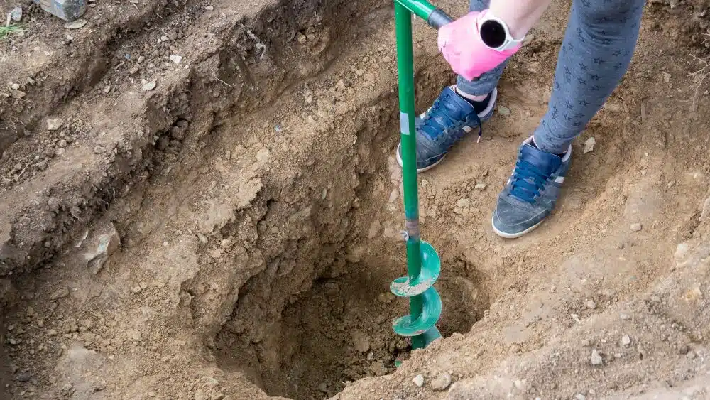 A green rod with spiral blades around the bottom digging a deep hole.
