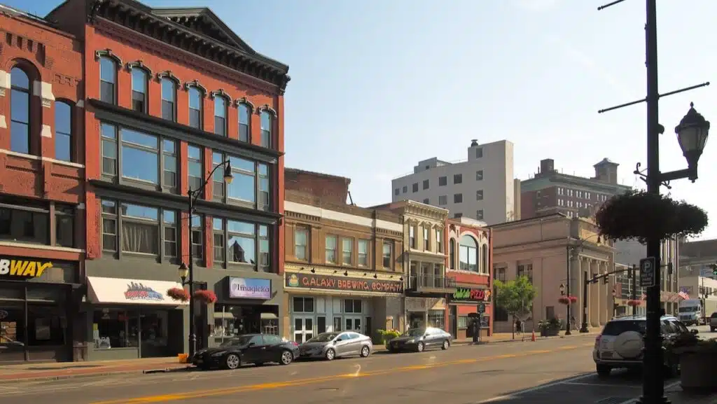 View of red-brick and brown-brick buildings on Court Street in downtown Binghamton New York. Businesses include a Subway on the far left, Galaxy Brewing Company in the middle and a pizza restaurant on the right