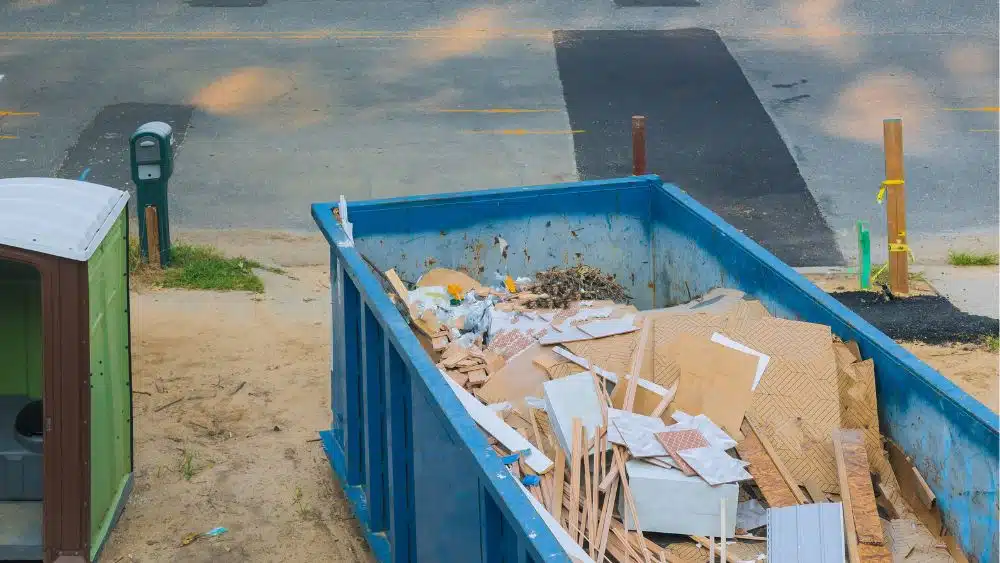Blue demolition dumpster filled with drywall and wood.