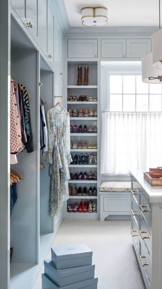 Walk-in closet painted a soft blue with a window letting in sunlight through sheer white curtains.