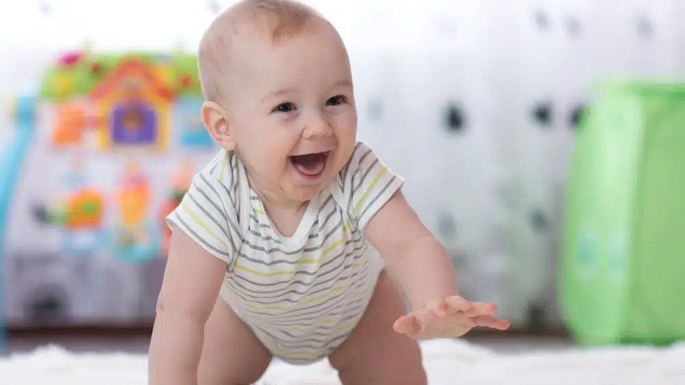 A smiling baby crawls and reaches toward the camera